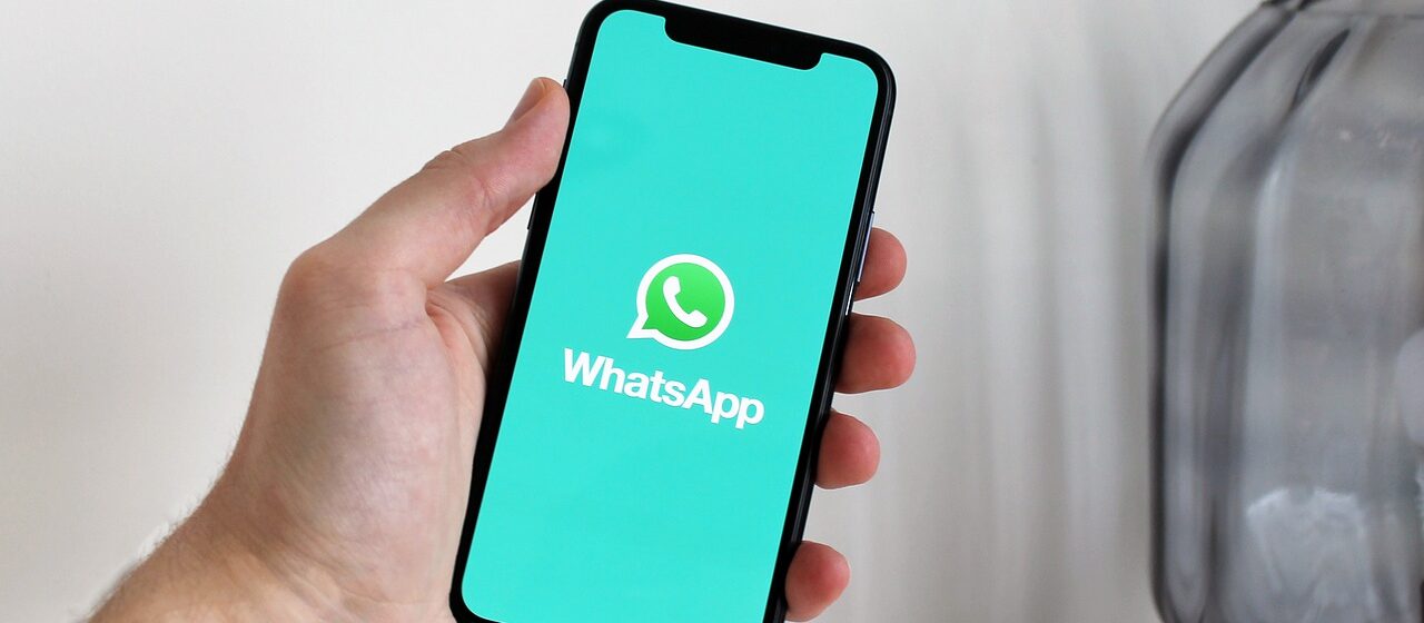 Uma mão segurando um smartphone que está mostrando o símbolo do WhatsApp.