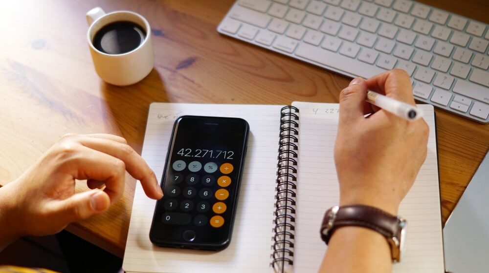 Uma mesa de trabalho com um celular aberto na calculadora e um caderno.